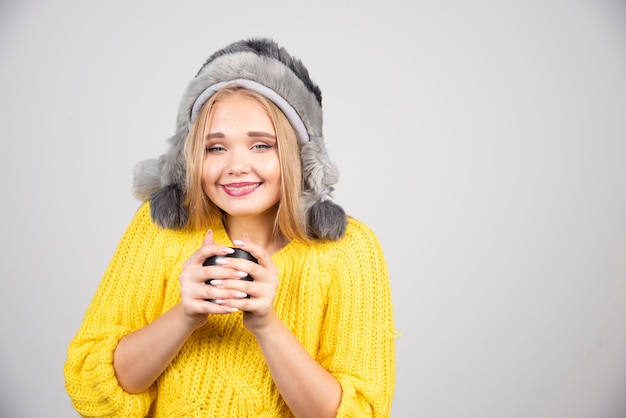 Mujer hermosa en suéter amarillo sosteniendo una taza de té.