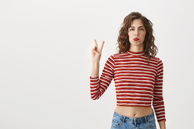 Mujer hermosa tonta haciendo pucheros y mostrando el signo de la paz