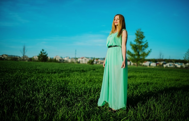 Mujer con un hermoso vestido largo turquesa posando en un prado sobre hierba