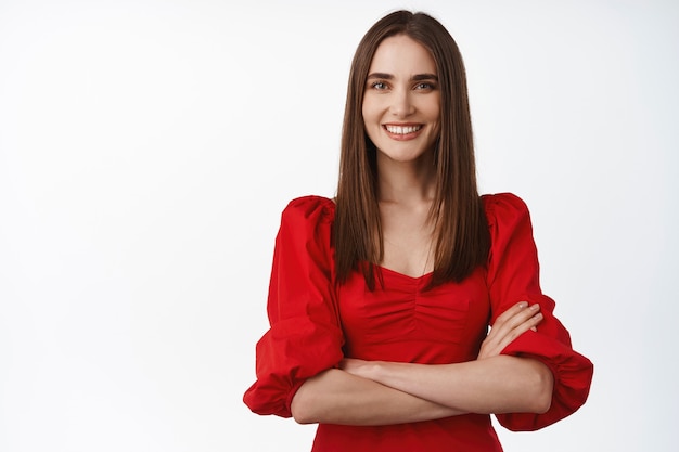 Mujer en un hermoso vestido rojo, brazos cruzados en el pecho confiada, sonriendo dientes blancos y luciendo determinada en blanco