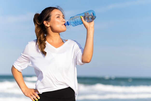 Mujer hidratada en la playa mientras hace ejercicio