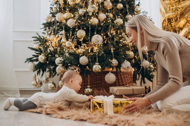 Mujer con hija sosteniendo regalos de Navidad por el árbol de Navidad