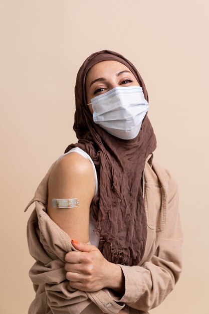 Mujer con hijab mostrando una pegatina en el brazo después de recibir una vacuna