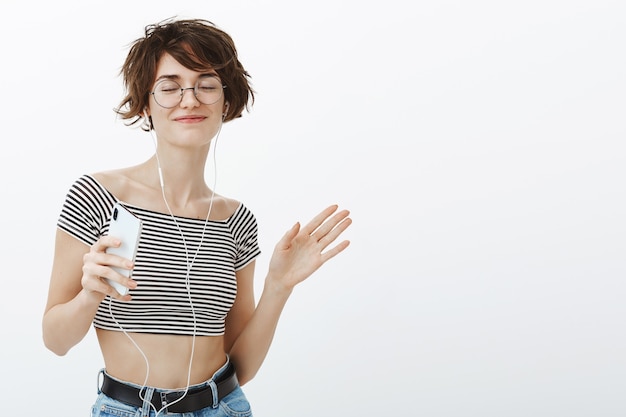 Foto gratuita mujer hipster atractiva despreocupada bailando y escuchando música en auriculares, sosteniendo smartphone