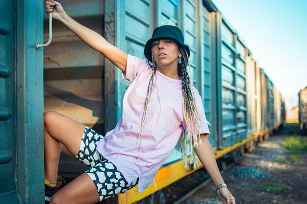 Una mujer hipster con estilo en un sombrero de cubo posando al aire libre en una antigua estación de tren