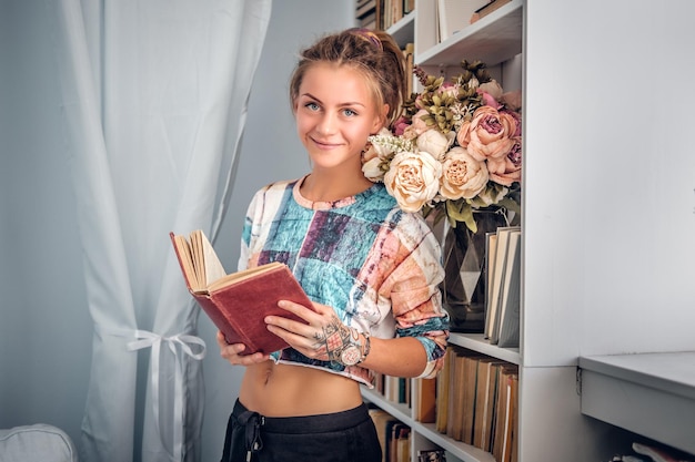 Mujer hipster positiva leyendo un libro cerca de puestos de libros.