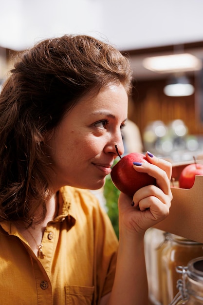 Foto gratuita mujer hipster que huele manzanas cultivadas en granjas biológicas en un almacén de residuos cero con baja huella de carbono. un cliente sonriente prueba para ver si las frutas de la tienda local del vecindario son frescas y no contienen químicos, de cerca