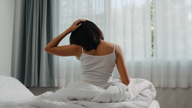 Mujer hispana adolescente se despierta en casa. La joven asiática que se estira después de dormir despierto toda la noche, comenzando un nuevo día con energía y vitalidad, se sintió muy renovada en la cama cerca de la ventana del dormitorio por la mañana.