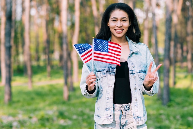 Mujer hispana con banderas de Estados Unidos mostrando gesto de paz.