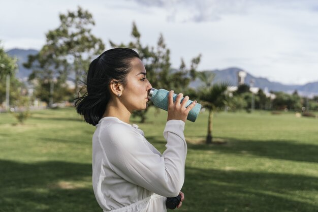 Mujer hispana descansando por agua potable después de la práctica de yoga