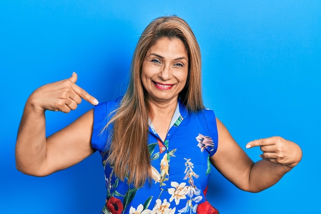 Mujer hispana de mediana edad con ropa informal que se ve segura con una sonrisa en la cara, apuntándose con los dedos orgullosa y feliz.