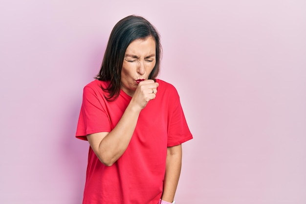 Mujer hispana de mediana edad con ropa informal sintiéndose mal y tosiendo como síntoma de resfriado o bronquitis. concepto de atención médica.