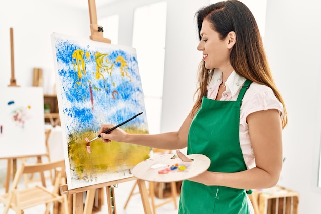 Mujer hispana de mediana edad sonriendo dibujo confiado en el estudio de arte