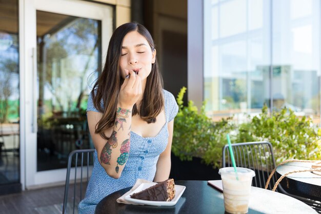 Mujer hispana satisfecha disfrutando de pasteles en el café en el centro comercial