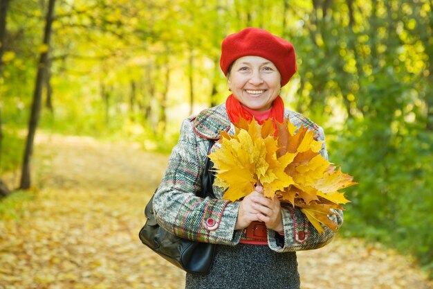 Mujer con hojas de arce en el parque de otoño