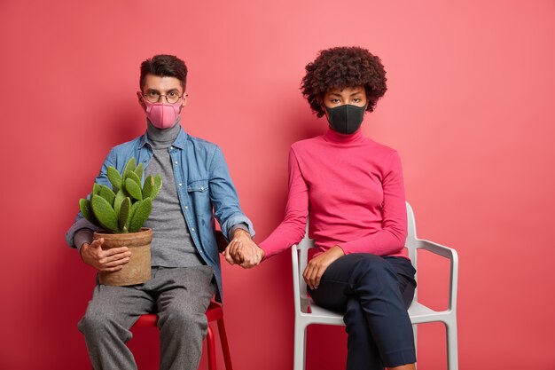 La mujer y el hombre casados infectados tienen el virus corona, usan máscaras protectoras y se toman de las manos, se sientan en sillas y se quedan en casa durante el autoaislamiento o la pandemia