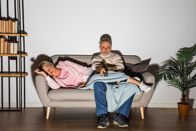 Foto gratuita mujer y hombre envejecidos con tv a distancia viendo la televisión en el sofá