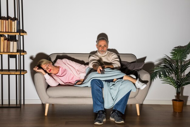 Mujer y hombre envejecidos con TV a distancia viendo la televisión en el sofá