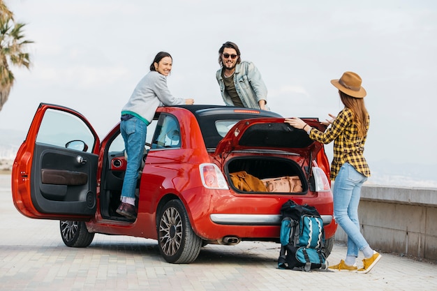 Foto gratuita mujer y hombre que se inclinan hacia fuera del auto cerca de la dama con la mochila cerca del maletero del auto