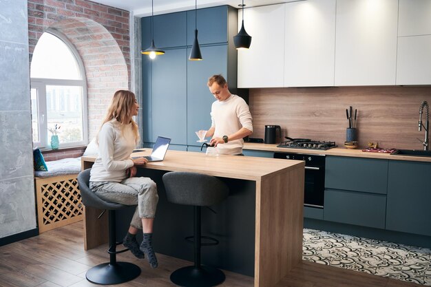 Mujer y hombre que trabajan en la computadora portátil en casa en la cocina moderna
