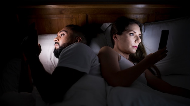 Mujer y hombre revisando sus teléfonos antes de dormir