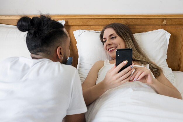 Mujer y hombre revisando sus teléfonos mientras está en la cama