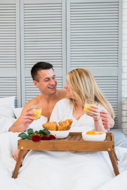 Foto gratuita mujer y hombre sonrientes con los vidrios en cama cerca de la comida en la mesa de desayuno