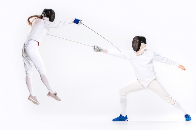 Foto gratuita la mujer y el hombre con traje de esgrima practicando con espada contra gris