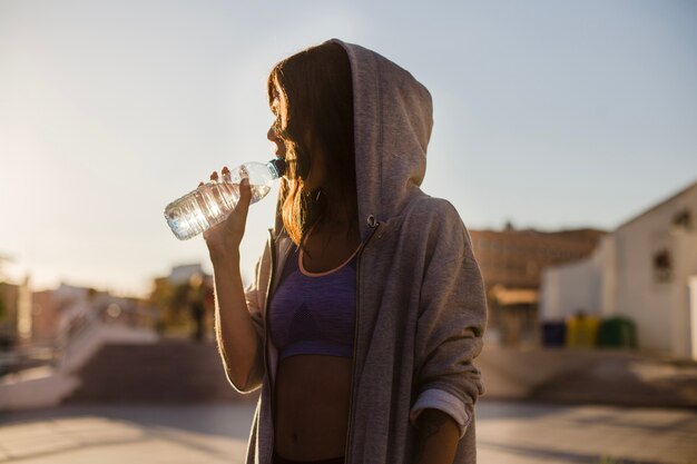 Mujer, hoodie, bebida, agua, posición, afuera