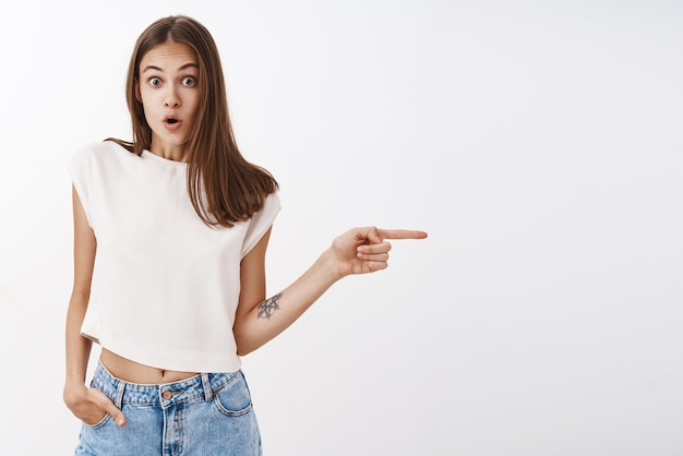 Mujer impresionada y sorprendida que hace preguntas sobre una exhibición increíble, está de gira por una ciudad extranjera con la mano en el bolsillo apuntando con los labios doblados hacia la derecha por el asombro y la curiosidad mirando