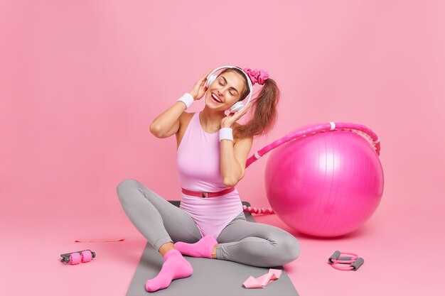 Mujer inclina la cabeza disfruta de su melodía favorita vestida con ropa activa lleva un estilo de vida activo y saludable ¿gimnasia o aeróbicos