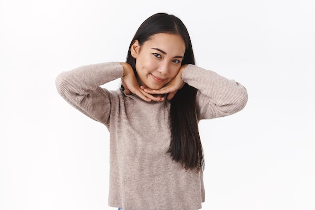 mujer inclina la cabeza linda, abraza la línea de la mandíbula y sonríe tontamente, luce coqueta o coqueta, mostrando su piel perfecta y limpia sin poros