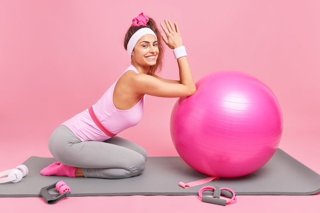 La mujer se inclina hacia la pelota de pilates inflada hace ejercicios en karemat satisfecho después de un entrenamiento productivo lleno de energía