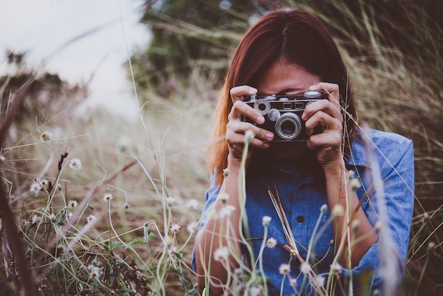 mujer inconformista joven que hace fotos con la cámara de película de época en el campo de verano. Las mujeres concepto de estilo de vida.