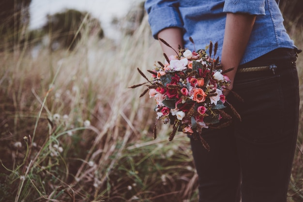 mujer inconformista joven que sostiene el ramo de rosas, mientras que disfrutar de un paseo en el campo de verano.