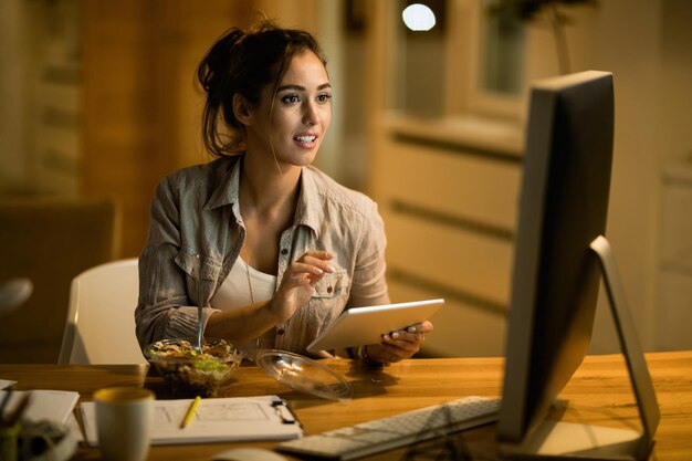 Mujer independiente que usa el panel táctil mientras lee el correo electrónico en la PC de escritorio por la noche en casa