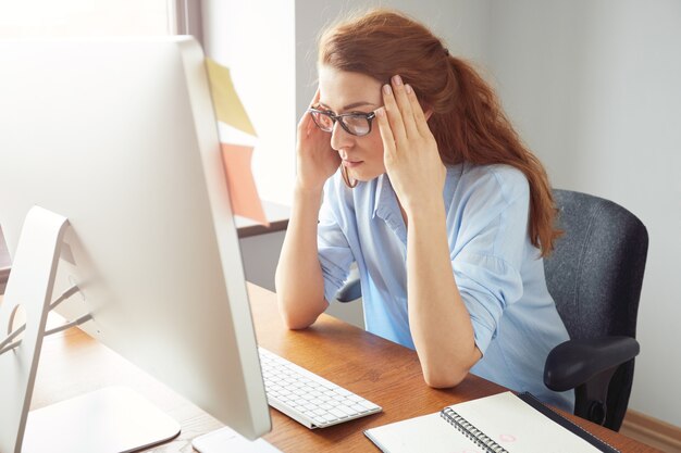 Mujer independiente segura sentada frente a la computadora con expresión seria y pensativa