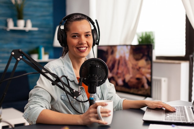 Mujer influyente sonriente sentada frente a cámara grabando video para blog de moda. Blogger digital vlogger streaming talk show en estudio con auriculares, micrófono de podcast profesional