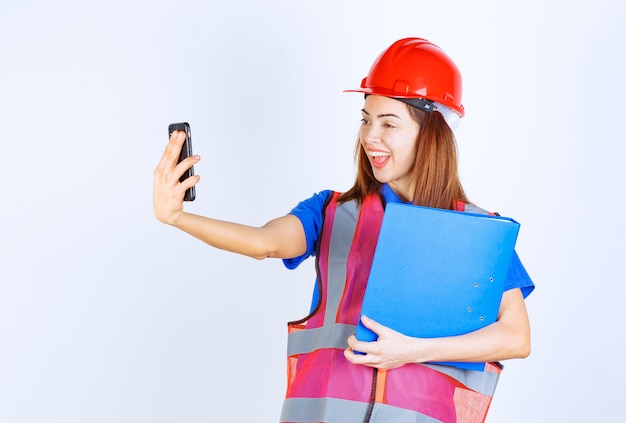 Mujer ingeniera en casco rojo revisando sus mensajes o haciendo una videollamada.