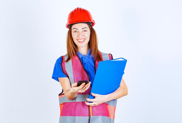 Mujer ingeniera en casco rojo revisando sus mensajes o haciendo una videollamada.