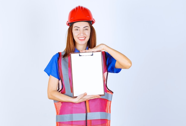 Mujer ingeniera en uniforme sosteniendo un archivo de informes en blanco.