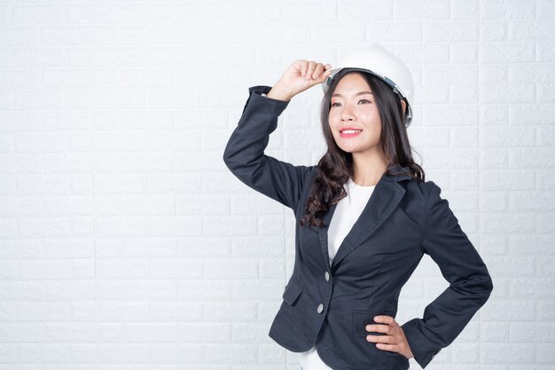 Una mujer de ingeniería que sostiene un sombrero, separa los muros de ladrillos blancos con lenguaje de señas.