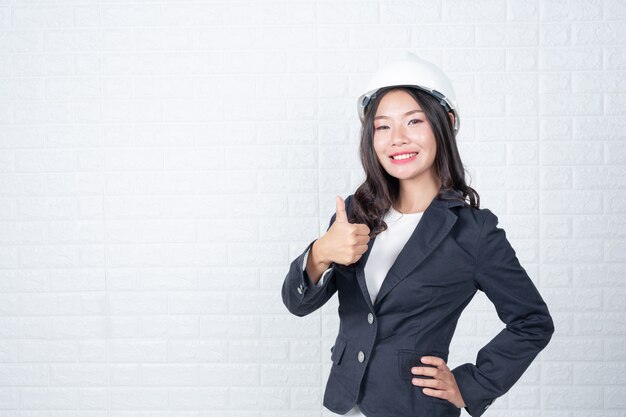 Una mujer de ingeniería que sostiene un sombrero, separa los muros de ladrillos blancos con lenguaje de señas.