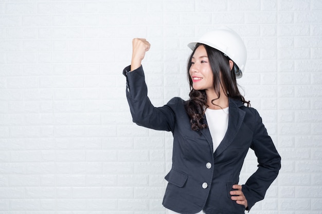 Una mujer de ingeniería que sostiene un sombrero, separa los muros de ladrillos blancos con lenguaje de señas.