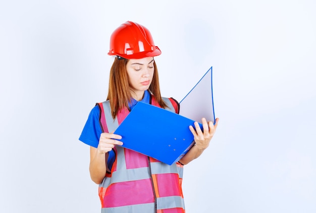 Mujer ingeniero en casco rojo sosteniendo una carpeta de proyecto azul.