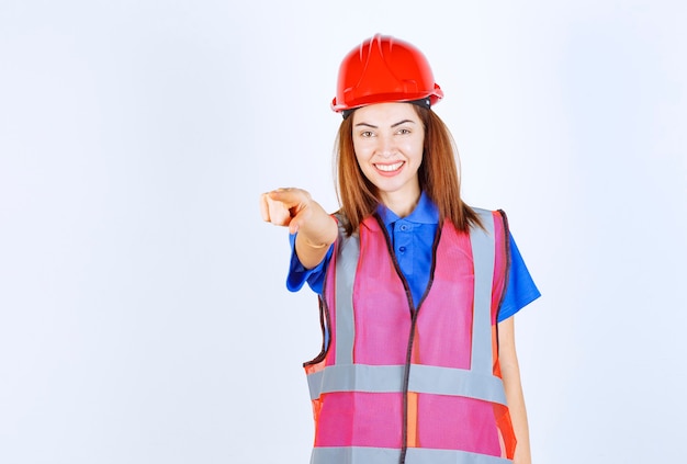 Mujer ingeniero en uniforme y casco rojo notando a la persona que está delante.