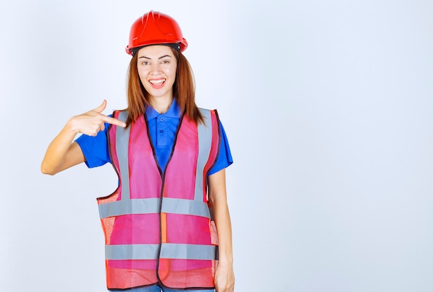 Mujer ingeniero en uniforme y casco rojo presentándose.