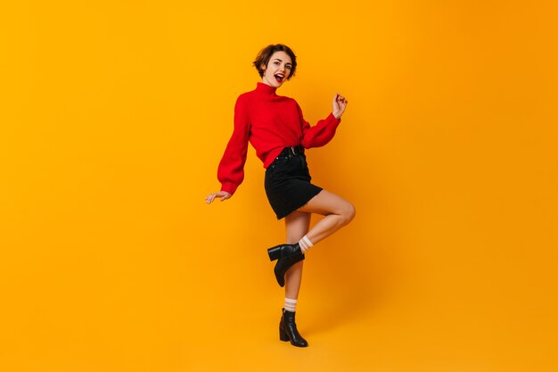 Mujer inspirada en falda corta bailando en la pared amarilla