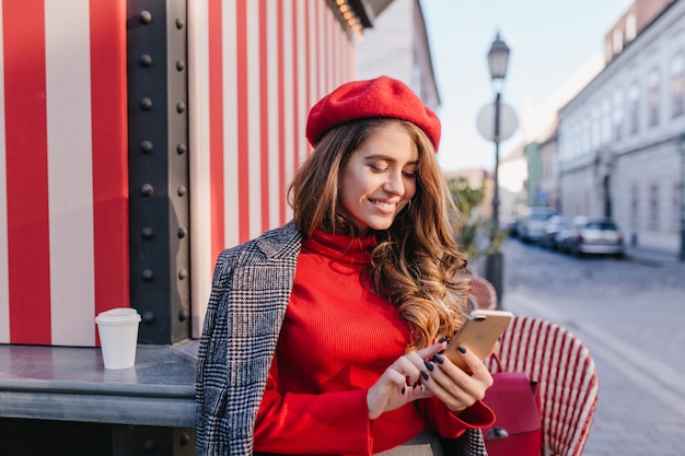 Mujer inspirada con mensaje de texto de expresión de rostro satisfecho mientras toma café cerca de la cafetería al aire libre