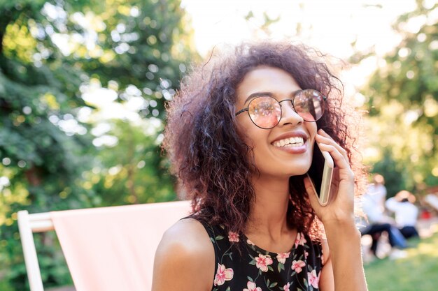 Mujer inspirada con pelos rizados relajantes en el parque de verano en fin de semana soleado.